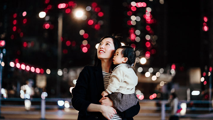 一位女士抱着孩子，抬头看着夜晚城市的灯光