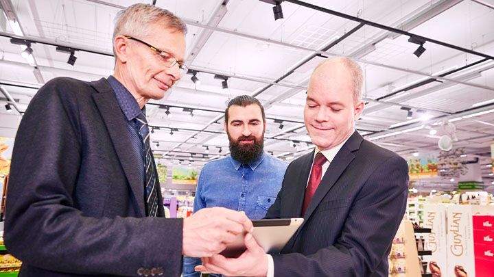 一家超市的三位经理低头微笑看着平板电脑