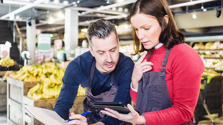 超市水果陈列架旁的两名同事正在讨论 iPad 上的数据